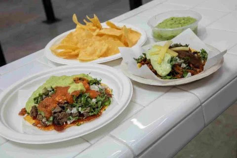 Tacos con carne, salsas, guacamole, cilantro y cebolla, acompañados de totopos.