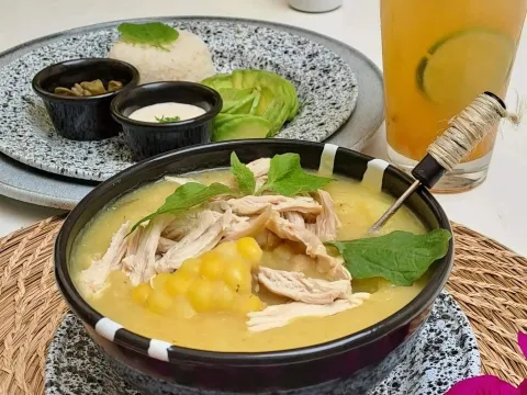 Ajiaco santafereño servido con pollo y papa, acompañado de arroz, aguacate, crema y otros complementos tradicionales.