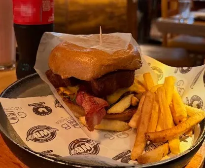 Hamburguesa con carne, queso y tocino, acompañada de papas fritas, servida en un plato de restaurante.