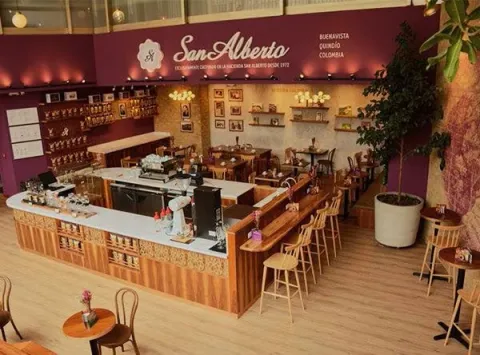 Espacioso café de San Alberto, con una barra central, mobiliario de madera y una decoración cálida que resalta su tradición cafetera.