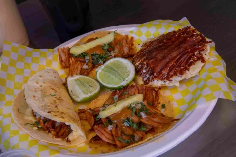 Plato con tacos al pastor, quesadilla, limón, pepino y salsas.