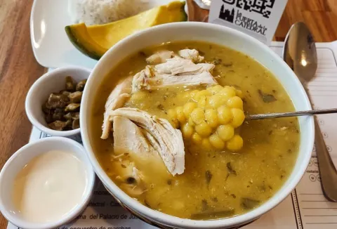 Ajiaco santafereño servido con pollo, mazorca y papa, acompañado de aguacate y alcaparras.