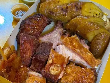 Plato con variedad de carnes asadas, acompañadas de plátano maduro y salsas, servido en una bandeja.