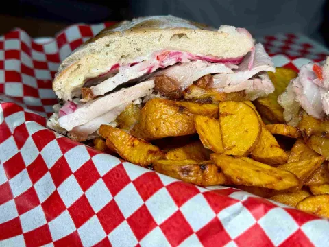 Sánduche de chicharrón con cebolla encurtida y papas doradas.
