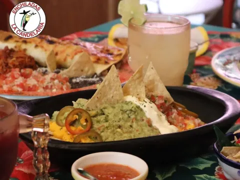 Nachos con guacamole, crema, queso, pico de gallo y jalapeños, acompañados de enchiladas y una bebida.