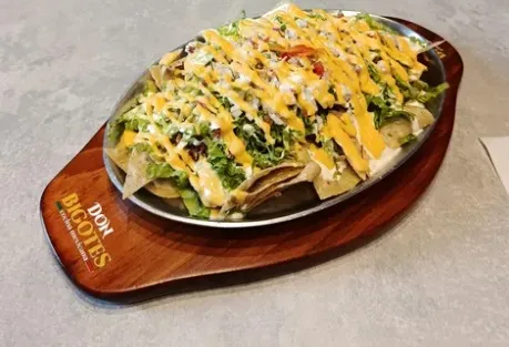  Nachos servidos con lechuga, frijoles y queso, cubiertos con salsa cremosa.