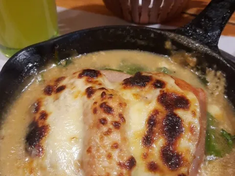Pollo gratinado con queso, servido en salsa cremosa en una sartén de hierro.