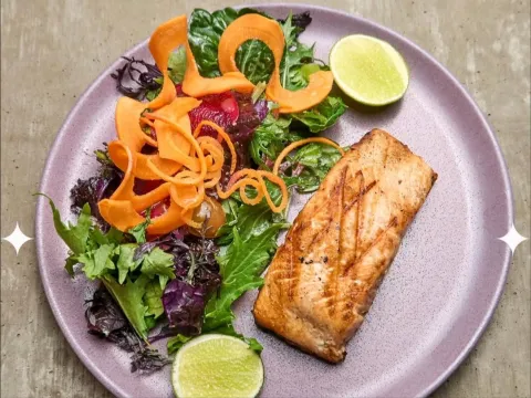 Filete de pescado a la parrilla acompañado de ensalada de hojas verdes, zanahoria en láminas, remolacha y rodajas de limón.