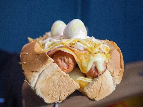 Perro caliente con salchicha, queso, salsas y toppings variados.