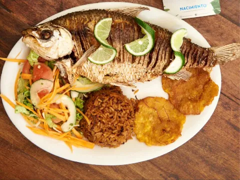 Pescado frito entero acompañado de arroz, patacones, ensalada fresca y rodajas de limón.