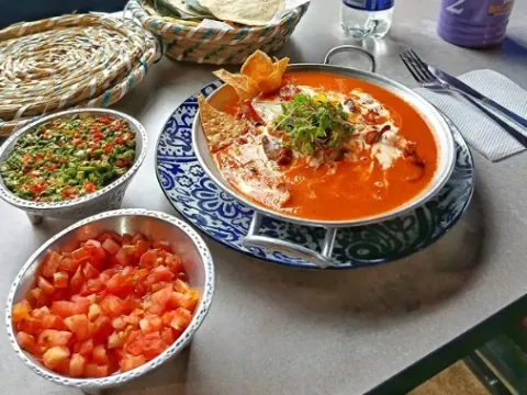 Enchiladas bañadas en salsa roja, acompañadas de guacamole y pico de gallo.