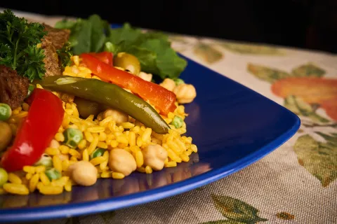 Plato de arroz con garbanzos, arvejas y pimentones, acompañado de vegetales frescos y una porción de proteína vegetal.