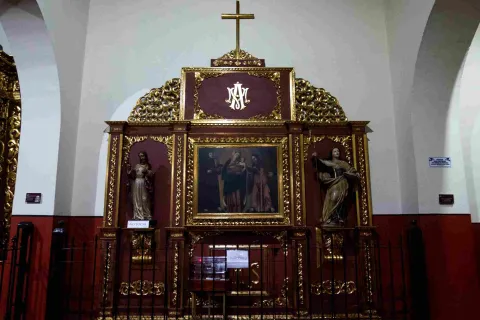 Retablo religioso con detalles dorados, una pintura central y dos figuras escultóricas, coronado por una cruz en el interior de la iglesia de San Juan de Dios.