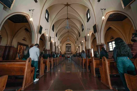 Interior de la iglesia de Monserrate, con sus arcos, vitrales, bancas de madera y visitantes en oración.