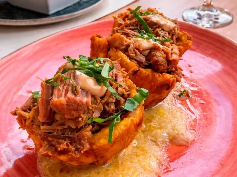  Plato de cerdo desmechado servido sobre una base crujiente con salsa.