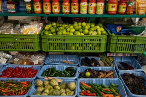 Puesto de mercado con canastas de limones, ajíes, tomatillos, especias, hierbas y salsas de diferentes variedades.
