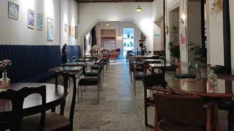 Pasillo largo de la cafetería con sofás de terciopelo azul, mesas de madera, cuadros modernos y plantas. 
