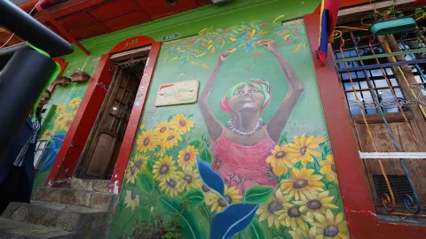 Detalle de mural en fachada verde con una mujer cosechando ajíes y el letrero de madera del restaurante. 