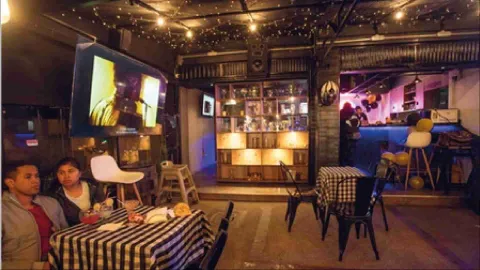 Pareja sentada en una mesa con mantel a cuadros disfrutando de bebidas en un bar con pantalla de televisión. 