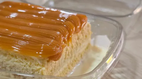 Porción de torta tres leches en envase plástico, cubierta con hilos de arequipe y bañada en salsa de leche. 