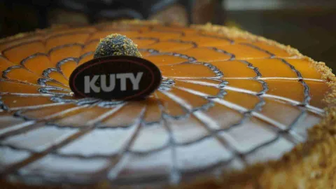 Plano detalle de una torta con glaseado de caramelo, decoración en telaraña y el sello del logo de Kuty. 
