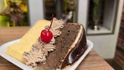 Porción de torta combinada de vainilla y chocolate con crema batida y una cereza en un plato desechable blanco.