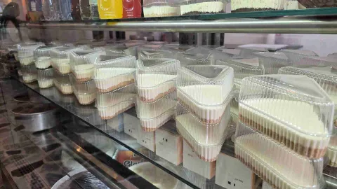 Múltiples porciones individuales de cheesecakes en envases plásticos triangulares apilados dentro de una vitrina.