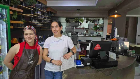 Dos colaboradoras sonríen detrás de la barra de atención del restaurante cerca del punto de pago. 