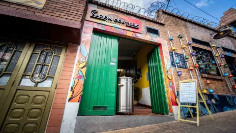  Vista en ángulo de la entrada del restaurante Sazón Costeño con letrero, marco decorado y tablero de menú.