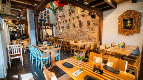  Comedor con mesas de madera, sillas azules, pared de ladrillo con artesanías precolombinas y cuadros dorados.