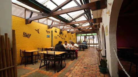 Patio interior cubierto con techo traslúcido, paredes amarillas y mesas ocupadas por comensales.