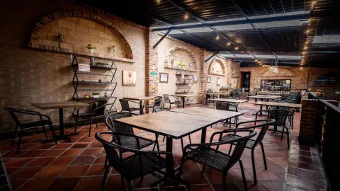 Salón de restaurante con paredes de ladrillo, arcos decorativos, suelo de terracota y mesas de madera con sillas negras.