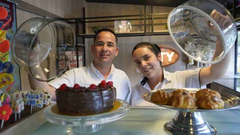  Dos empleados de Kuty levantando campanas de vidrio para mostrar tortas de chocolate y panecillos. 