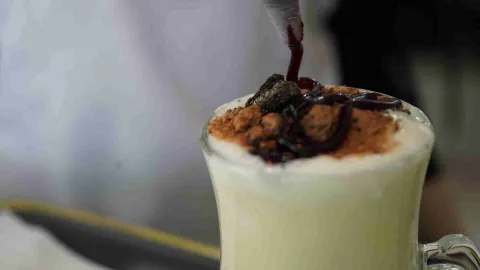 Plano detalle de un postre en copa decorado con canela, galleta y salsa de mermelada servida con manga. 