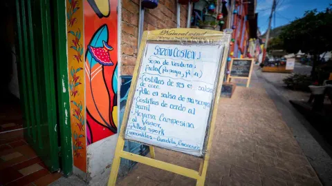 Tablero informativo de madera con el menú del día escrito a mano en la entrada del restaurante Sazón Costeño.