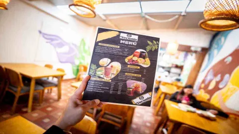  Mano sosteniendo la carta de menú impreso del restaurante Yoconta en el interior del comedor con luz cálida.