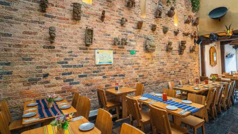 Pared de ladrillo expuesto decorada con esculturas precolombinas y mesas de madera servidas con caminos de mesa.