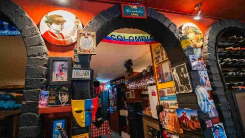Entrada a salón con arcos de ladrillo, banderas, fotos temáticas de Argentina y Colombia, y máscaras decorativas.