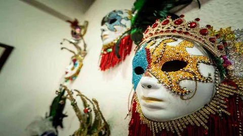 Primer plano de máscaras ornamentadas con pedrería y plumas de colores vibrantes, colgadas como decoración en una pared.