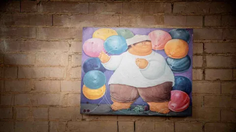 Cuadro al óleo sobre pared de ladrillo que representa a un chef de estilo volumétrico sosteniendo hilos de globos de colores.