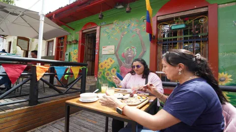 Dos mujeres almorzando en una mesa de madera en la terraza exterior del restaurante Peri Peri. 