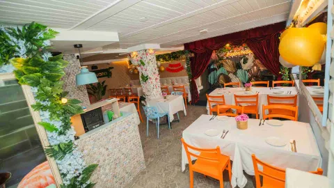 Vista amplia del salón con columnas florales, mesas vestidas de blanco, sillas naranjas y un escenario al fondo.