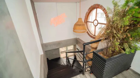 Escalera de madera oscura con barandilla metálica, lámpara tejida, maceta con vegetación y letrero luminoso de Aperol Spritz.