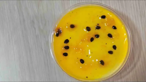 Vista superior de mousse de maracuyá en vaso cilíndrico, cubierto con gelatina amarilla y semillas de la fruta. 