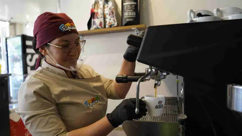 Barista preparando un café espresso en máquina profesional mientras sirve la bebida en una taza blanca. 