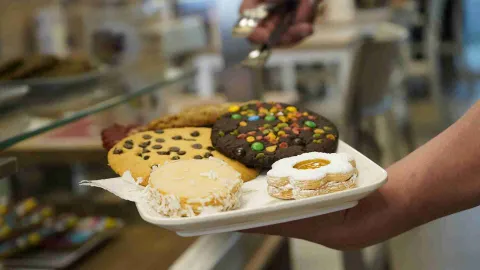 Persona sosteniendo un plato blanco con galletas surtidas de chispas de chocolate, confites y mermelada. 