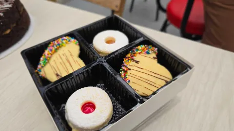Caja organizadora negra con galletas de mantequilla en forma de corazón con chispas de colores y alfajores. 