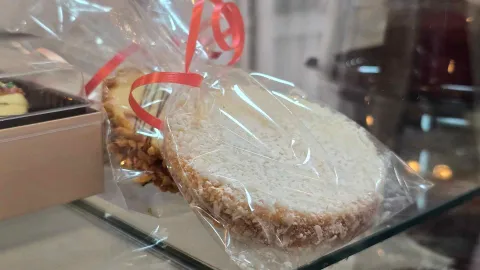  Alfajor redondo espolvoreado con coco rallado, empacado en bolsa transparente con una cinta roja de regalo. 