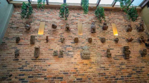 Pared de ladrillo con réplicas de figuras arqueológicas precolombinas alineadas y plantas colgantes en el techo.