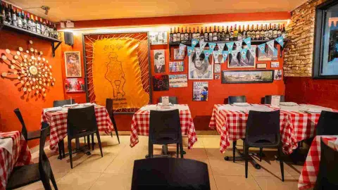 Salón de restaurante con mesas vestidas con manteles a cuadros rojos, paredes rojas y adornos de cumpleaños.